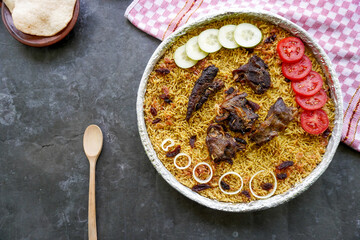 Traditional Kebuli Rice with Lamb, aromatic spiced rice dish cuisine, served with tender meat, raisins, cucumber, onion, seasoning and fresh tomato slices