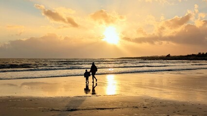 Mother and child walking on Silverstrand Beach Galway Ireland during sunset, family love, bonding, travel, ocean reflection, nature, and peaceful lifestyle