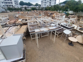 Chaotic outdoor junkyard filled with large pile of old, abandoned, and damaged furniture. Tables, chairs, and desks in disarray create scene of neglect and waste