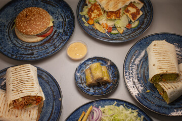 A variety of fast food items is beautifully arranged on dark blue plates, featuring wraps, a burger, and sides to enjoy