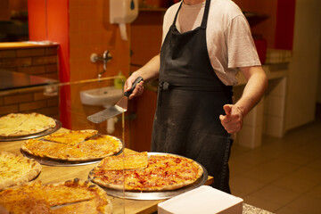 In a bustling restaurant kitchen, a man wearing an apron serves delicious pizza slices to customers