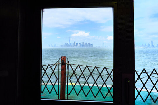 Fototapeta Manhattan skyline seen through the doors of Staten Island Ferry with ocean waves in the foreground.