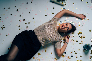 Happy woman celebrating lying on floor with confetti