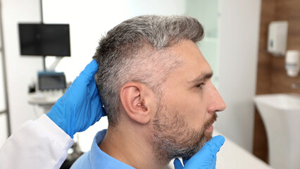 Fototapeta premium Doctor audiologist applying hearing aid to mature man's ear. Hearing-impaired man needs hearing aids