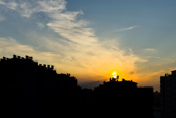 Obraz premium Sunset over urban skyline with silhouetted buildings and warm sky