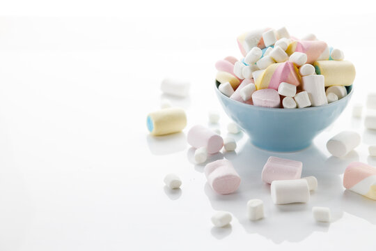 Colorful marshmallows in a bowl on white table background.