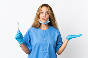 Woman dentist holding tools isolated on white background having doubts while raising hands
