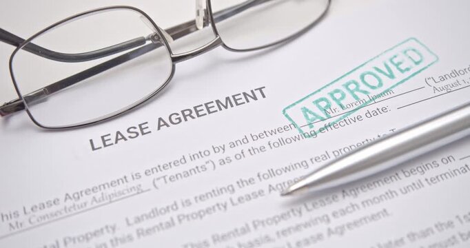 Green APPROVED stamp on lease agreement paper beside pen and eyeglasses, representing successful property rental, contract approval, and official business process.