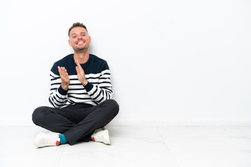 Young man sitting on the floor isolated on white background applauding after presentation in a conference