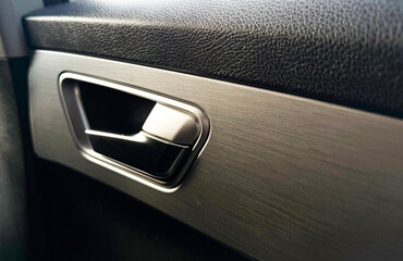 Macro view of a car door handle featuring brushed aluminum finish and black leather texture. The sleek design, fine details, and lighting emphasize modern automotive craftsmanship and luxury interior 