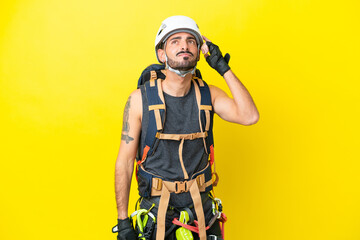 Young caucasian rock climber man isolated on yellow background having doubts and with confuse face...