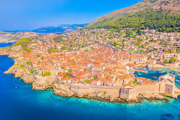 Drone photo of Dubrovnik showing the fortified old town with stone walls, terracotta rooftops, Adriatic coastline, harbor and stunning UNESCO World Heritage medieval architecture