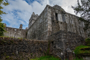 The ruins of Muckross Abbey, Ireland, with multiple levels and arched windows, surrounded by greenery under a partly cloudy sky