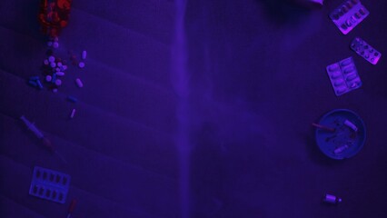 Pills, cigarettes and syringe under neon light