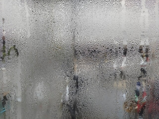 A close-up of a windowpane completely covered in tiny condensation droplets, with vertical streaks and a muted grey quality.