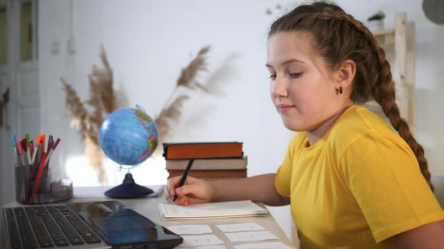 Girl studying at desk with globe laptop book pencil braid doing homework and school study on notebook near stack of book and pen cup educational focus concentration and calm learning environment