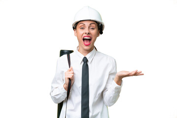 Young architect woman with helmet and holding blueprints over isolated background with shocked facial expression