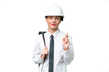 Young architect woman with helmet and holding blueprints over isolated background with fingers crossing and wishing the best