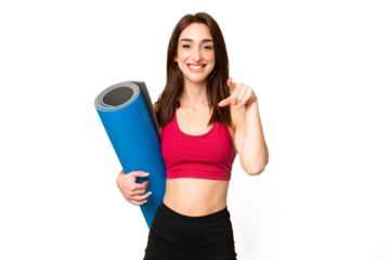 Young sport caucasian woman going to yoga classes while holding a mat over isolated chroma key background surprised and pointing front