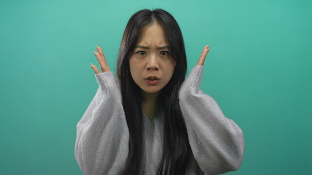 Young chinese woman in gray sweater expressing emotion against isolated green background wall.
