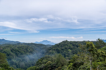 Scenic view of rolling hills and distant mountains under a blue sky, captured from Panorama Baru in Bukittinggi, West Sumatra.