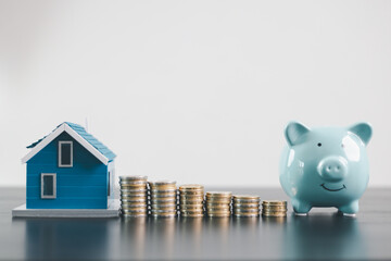Mini house model with coins and blue piggy bank, representing mortgage loan, real estate...