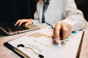 Business analysis with medical interpretation concept using stethoscope and charts on desk with laptop background in office setting