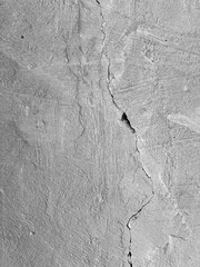 Dramatic black and white shot: a wide, winding crack cutting across the rough, shadow-covered surface of an old wall.