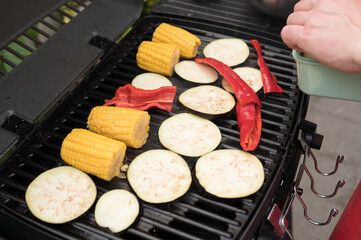 Grilling eggplant, corn, and red peppers on outdoor barbecue