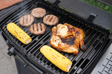Grilled chicken and beef burgers with corn on charcoal bbq