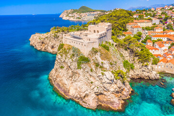 Drone image of Dubrovnik showing a majestic cliffside fort overlooking the turquoise Adriatic Sea, rugged coastline, stone walls and breathtaking Mediterranean scenery