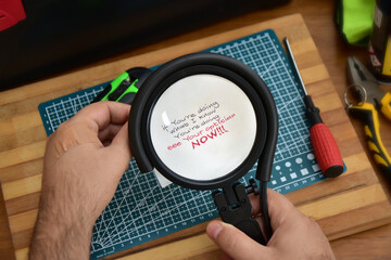 Man in workshop magnifying small text on a note that advises him to visit an ophthalmologist if he can't see
