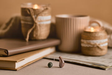 BTE hearing aid rests on a table beside cozy candles, coffee, and books, symbolizing hearing health and connection