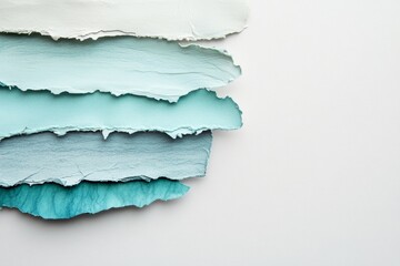 Fototapeta premium Layered torn paper pieces create a subtle gradient of cool teal and light blue hues against a plain white background.