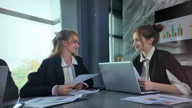 Business meeting in office with two women discussing reports and graphs