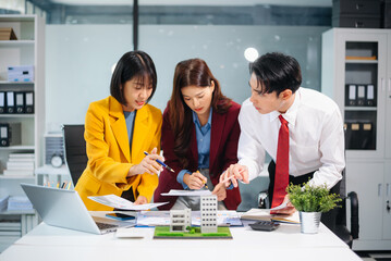 Asian team collaborating on real estate and architecture projects with blueprints, models, and data charts in a modern office, showcasing business teamwork and success.
