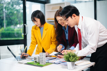 Asian team collaborating on real estate and architecture projects with blueprints, models, and data charts in a modern office, showcasing business teamwork and success.