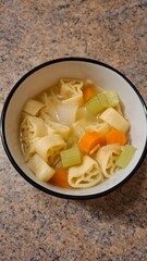 Top-view bowl of rotelle pasta soup with carrot (Daucus carota) and celery (Apium graveolens) in a clear homemade broth — cozy flatlay for recipes, food blogs and marketing.
