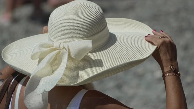 Woman, sun hat, summer. Woman adjusting wide-brimmed white straw hat on a bright sunny day outdoors.