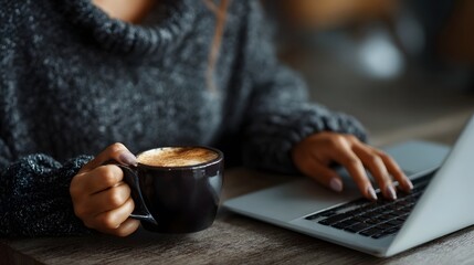 A focused person typing on a laptop with a warm cup of coffee in hand working remotely from a cozy cafe setting