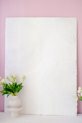 Textured white wall art with circular patterns, complemented by a minimalist vase of fresh flowers, creating a serene and stylish interior decor atmosphere. Copy space