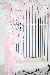 Elegant decorative birdcage adorned with white leaves and pink accents, featuring a plush fur seat, creating a serene and inviting atmosphere for interior design