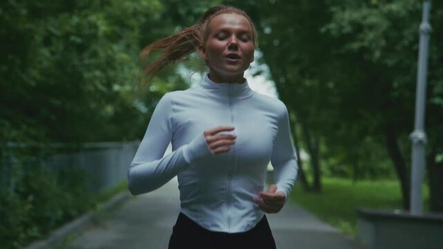 A determined runner breathes through the challenges of her workout, showcasing her dedication and perseverance in a lush, green park setting.