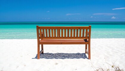 A lone bench faces turquoise waves under a clear sky on a sunlit white beach.