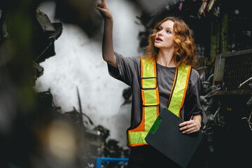 Female technician checking used car engine block sale order at scrapyard warehouse recycle area...
