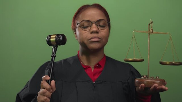 Serious african american judge holds gavel and scales in green studio setting with eyes closed; authority.