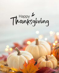 Festive Thanksgiving composition with pumpkins, autumn maple leaves, and holiday lights. Seasonal fall decoration background with Happy Thanksgiving text for greeting cards, posters