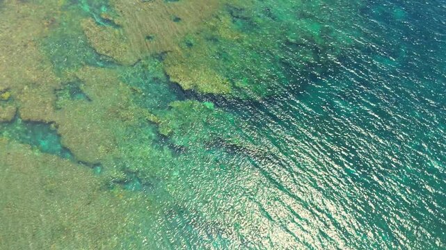 Aerial view of vibrant turquoise ocean water with visible shallow coral reefs and surfboats, Siargao, Philippines.