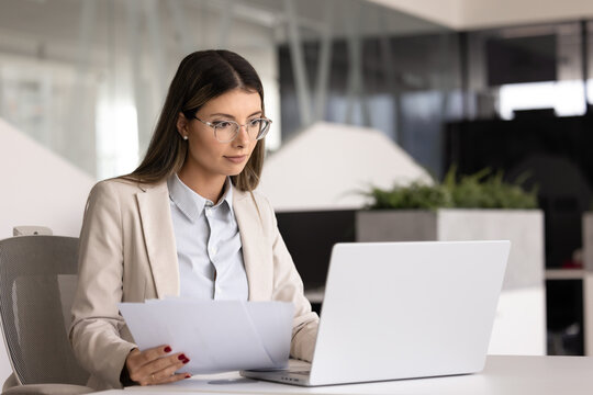 Serious Hispanic company accountant woman in glasses working at laptop