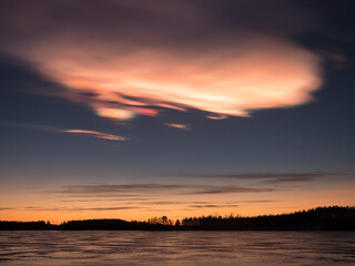 Nacreous cloud in the sky behind frozen lake